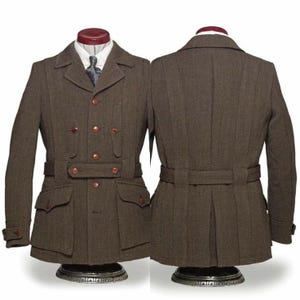 Puede incluir: Chaqueta de lana marrón con doble botonadura, con cuatro botones y dos bolsillos con solapa. La chaqueta tiene cinturón en la cintura y se exhibe en un maniquí. También se ve la parte trasera de la chaqueta.