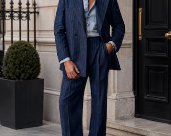 Puede incluir: Un traje azul marino con rayas finas, con una chaqueta cruzada y pantalones de pernera ancha. El traje se lleva sobre una camisa vaquera azul claro. La persona lleva zapatos de cuero marrón. El escenario es al aire libre, frente a un edificio.