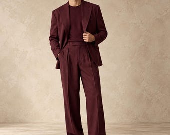 May include: A deep burgundy suit consisting of a single-breasted blazer with wide lapels and matching pleated trousers. The ensemble is paired with a coordinating burgundy crew-neck shirt and dark brown leather loafers, creating a monochromatic look.
