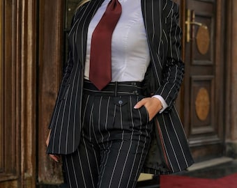 Op de afbeelding: Een zwart-wit krijtstreep pak met een wit overhemd en een bordeauxrode stropdas. Het pak bestaat uit een blazer en een broek met hoge taille. Een zwarte fedora hoed maakt de look compleet. De tekst "Mariclothing" staat onderaan.