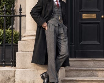 Vintage driedelig herenpak uit de jaren 1920 met lange zwarte overjas, grijs tweed vest en geplooide broek, een trouwpak geïnspireerd op Peaky Blinders.