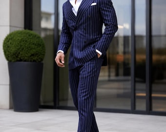May include: A navy blue double-breasted suit with white pinstripes, paired with a white dress shirt and black leather loafers. The suit features a pocket square and is worn with sunglasses. The outfit is a classic business or formal wear ensemble.