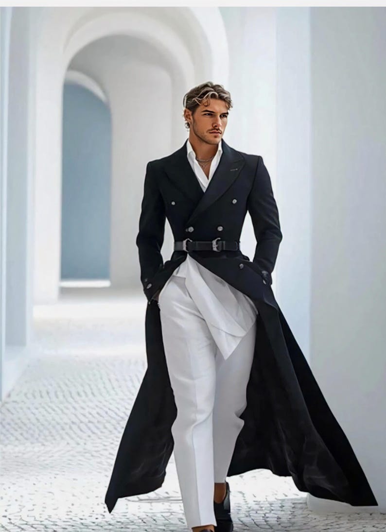 May include: A long, black double-breasted overcoat, paired with a white shirt and trousers, and a black belt. The outfit is completed with black shoes. The image is taken in a white hallway. The coat's length is a key feature.