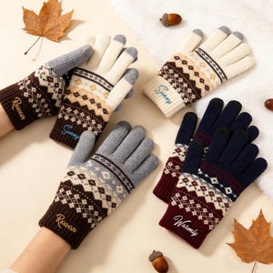 Puede incluir: Cuatro pares de guantes de punto con patrones de estilo fair isle en varias combinaciones de colores, incluyendo marrón, crema, gris y azul marino. Cada par tiene bordados nombres como Rowan, Sunny o Warmly en los puños acanalados.