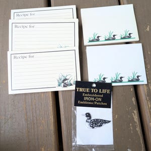 May include: Three white recipe cards with black borders and lines, featuring the text "Recipe for" and a graphic of a loon in green grass. Two white note cards with a green loon graphic. One black and white embroidered loon iron-on patch.