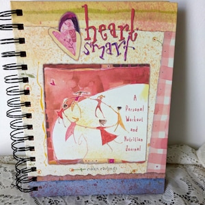 May include: Spiral-bound journal with the title "heart smart" in red and purple lettering. The cover features a watercolor illustration of figures dancing and the text "A Personal Workout and Nutrition Journal". The journal has a decorative heart design.