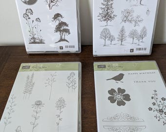May include: Four clear plastic cases containing rubber stamp sets by Stampin' Up. The sets feature black ink illustrations of trees, flowers, birds, butterflies, and text including Happy Birthday and Thank You, organized in grid layouts.