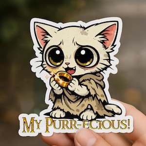 Pode incluir: Um adesivo com um gato de desenho animado com olhos grandes, segurando um anel de ouro. O gato está usando uma capa com capuz e o texto "MY PURR-ECIOUS!" está abaixo. O gato é creme com detalhes em rosa.