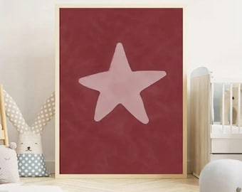 Può includere: Una stampa incorniciata con una grande stella rosa chiaro su uno sfondo rosso scuro. La stella ha un aspetto disegnato a mano. La cornice è in legno chiaro. L'opera d'arte si trova in una cameretta.