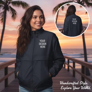 May include: A navy blue windbreaker jacket with a full front zipper and a small white text box that says "YOUR DESIGN HERE". The jacket is shown on a person standing on a wooden dock with a sunset in the background. The jacket is also shown in a circular inset.