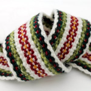 May include: A woven ribbon with a colourful geometric pattern. The ribbon features a repeating design of red, green, yellow, and white stripes. The ribbon is rolled up, showcasing its texture and design. The edges are finished with a white border.