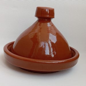 Peut inclure: Un tajine en céramique marron vernissé, avec un couvercle conique et une base large et peu profonde. Le tajine est un plat traditionnel d'Afrique du Nord, conçu pour la cuisson lente. Le pot a une finition brillante et est adapté à la cuisson sur la cuisinière ou au four.