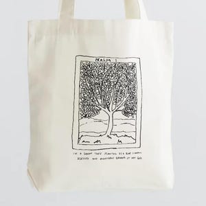 Könnte beinhalten: Cremefarbene Tragetasche mit einer Schwarz-Weiß-Illustration eines Baumes in einem rechteckigen Rahmen. Der Text "Psalm 1" befindet sich über dem Bild, darunter Schrift. Die Tasche hat zwei Griffe.
