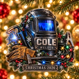 May include: A decorative Christmas ornament featuring a welding helmet with the text COLE WELDER, a welding torch, a brown leather glove, a hammer, and coiled cables with colorful lights, accented by pine branches, red berries, and snowflakes.