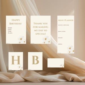 Könnte beinhalten: Eine Sammlung cremefarbener Schreibwaren mit goldenem Text und floralen Akzenten. Enthält eine "Happy Birthday"-Karte, eine "Thank You"-Karte, einen Menüplaner und Buchstabenkarten "HB". Das Design ist weich und elegant.