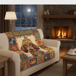 Può includere: Una coperta decorativa con un bassotto che indossa un cappello e una sciarpa di lana. La coperta ha un design patchwork con la scritta "DACHSHUND" in alto. La tavolozza dei colori comprende marrone, blu, rosso e giallo. La coperta è drappeggiata su un divano bianco.