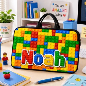 Könnte beinhalten: Eine rechteckige Laptoptasche mit einem bunten Muster aus ineinandergreifenden Kunststoff-Bausteinen in Rot, Gelb, Blau und Grün. Der Name Noah ist in großen, blockartigen Buchstaben in der Mitte der Tasche aufgedruckt.