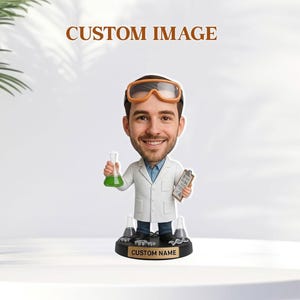 Può includere: Statuetta bobblehead di uno scienziato sorridente con occhiali e camice da laboratorio, che tiene in mano un pallone con liquido verde e un blocco per appunti. La base ha il testo "CUSTOM NAME" e le parole "CUSTOM IMAGE" sono sopra.