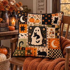 Könnte beinhalten: Ein quadratisches Zierkissen mit Patchwork-Design und Halloween-Motiven, darunter ein weißes Gespenst, das eine schwarze Katze hält, Kürbisse, Mondsicheln, Sterne, Fledermäuse und Blumenmuster in Orange, Schwarz und Grün mit schwarzer Paspelierung.