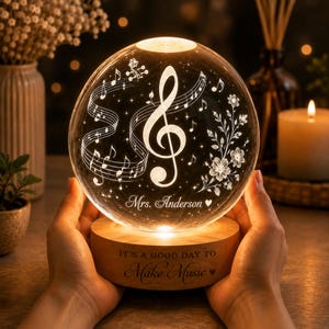 May include: A spherical glass night light featuring an etched treble clef, musical notes, and floral patterns. The glass sphere displays the text Mrs. Anderson. The wooden base is engraved with the text IT'S A GOOD DAY TO Make Music.