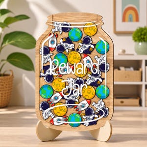 Puede incluir: Un frasco de recompensas de madera con forma de tarro, con un diseño temático del espacio que incluye ilustraciones coloridas de astronautas, cohetes, planetas y lunas. Las palabras Reward Jar están impresas en blanco en el centro.