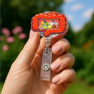 May include: A red and orange intestine-shaped badge reel with cartoon food and pill graphics. The badge reel has a clear plastic retractable cord and a clear plastic clip.