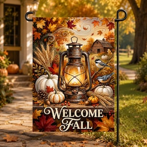 May include: A rectangular garden flag featuring a lit lantern, white pumpkins, wheat stalks, pinecones, and two birds perched on a branch. A rustic barn sits in the background amidst autumn leaves. The text WELCOME FALL is printed in white.