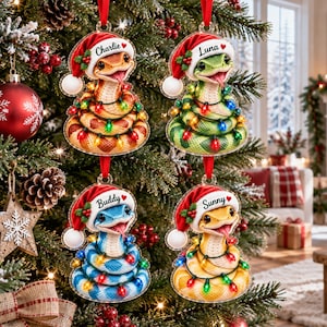 Könnte beinhalten: Vier flache Acryl-Weihnachtsanhänger in Form von geringelten Schlangen mit roten Weihnachtsmützen und Stechpalmen. Jede Schlange ist mit bunten Lichterketten umwickelt und mit einem Namen versehen: Charlie, Luna, Buddy oder Sunny.