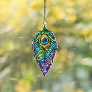 Puede incluir: Un colgante de pluma de pavo real colorido con una cadena plateada. El colgante presenta un diseño vibrante con tonos de azul, verde, amarillo y morado. El colgante mide aproximadamente 10 cm de largo.