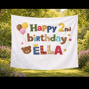 Pode incluir: Bandeira branca com o texto "Happy 2nd birthday ELLA" em letras de patchwork coloridas. A bandeira inclui um ursinho de pelúcia, balões, estrelas e uma coroa. A bandeira está pendurada ao ar livre em frente a um fundo verde.