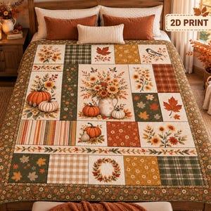 Pode incluir: Uma colcha de retalhos com design de outono com abóboras, girassóis, folhas, pássaros e padrões xadrez em tons de laranja, castanho, verde e creme. A colcha exibe um arranjo floral central e uma etiqueta com o texto 2D PRINT.