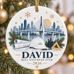 Op de afbeelding: Een rond wit keramieken ornament met een stadsgezicht, een tuibrug, een witte veiligheidshelm met de tekst CIVIL ENGINEER, opgerolde bouwtekeningen, een potlood en een geodriehoek. Tekst: DAVID, BEST ENGINEER EVER, 2026.