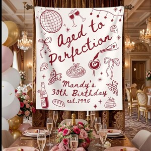 May include: A white banner with burgundy illustrations and text that reads "Aged to Perfection" and "Mandy's 30th Birthday est.1995". The banner features images of wine glasses, grapes, and a cake.