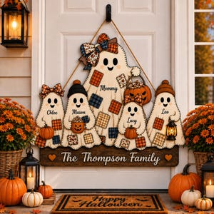 May include: A wooden door sign featuring five ghost figures with plaid patches, bows, and hats. The ghosts are labelled Mommy, Chloe, Mason, Lucy, and Leo. A dark wooden base plate at the bottom displays the text The Thompson Family with two hearts.