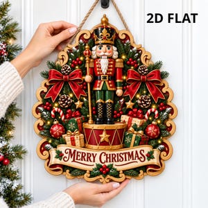 May include: A 2D flat decorative wall hanging featuring a central nutcracker figure standing on a drum, surrounded by pine branches, red bows, pinecones, candy canes, and gift boxes. A banner at the bottom displays the text Merry Christmas.
