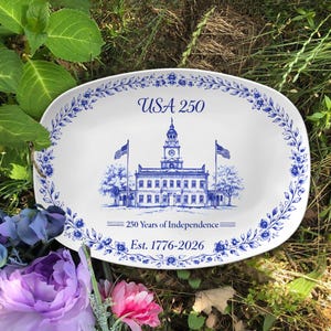May include: White oval serving platter with a blue floral border and a blue illustration of a building with flags. The platter has the text "USA 250" and "250 Years of Independence Est. 1776-2026".