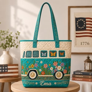 May include: A quilted tote bag featuring a teal van design with colorful floral patterns and butterflies. The upper section is cream-colored with a quilted texture. The name Ema is embroidered in white script at the bottom. It has two teal handles.