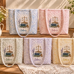 Puede incluir: Cinco bolsos tote acolchados en azul claro, rosa, verde salvia, lavanda y amarillo, cada uno con un patrón floral y un diseño bordado de una balanza de justicia sobre libros con el nombre Selena cosido debajo en letra cursiva.