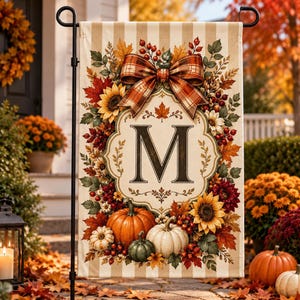 May include: A vertical garden flag featuring a beige and white striped background with a central ornate frame containing the letter M. The design is decorated with autumn foliage, sunflowers, red berries, and pumpkins, topped with a plaid bow.