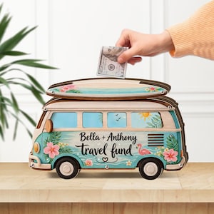 May include: A wooden travel fund bank shaped like a vintage van, with a surfboard on top. The van is teal and cream, decorated with floral and tropical designs. The text "Bella + Anthony travel fund" is displayed on the side.