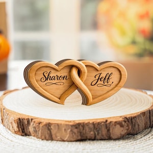 May include: Wooden heart-shaped decor with the names "Sharon" and "Jeff" engraved on each heart. The two hearts are interlocked, and the decor is placed on a wooden slice.