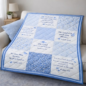 以下が含まれることがあります： 花柄とインスピレーションを与える聖書の引用句が特徴の、青と白のキルトスローブランケット。ブランケットはダイヤモンドパターンと青い縁取りが特徴です。テキストには、箴言、イザヤ、詩篇からの詩が含まれています。