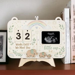 May include: A wooden pregnancy countdown calendar showing "32" weeks remaining. The design includes a rainbow, elephants, and the text "Weeks Until We Meet You" and "little one."