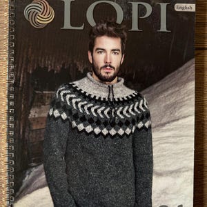 Può includere: Un libro a spirale con la parola "LOPI" in grandi lettere grigie. La copertina presenta un uomo con un maglione grigio e nero a fantasia. La parola "English" è nell'angolo in alto a destra. Il numero "34" è nell'angolo in basso a destra.