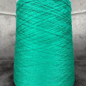 Puede incluir: Una gran bobina de hilo verde azulado vibrante. El hilo está bien enrollado, creando una forma cónica. La textura del hilo es visible, con hebras individuales que forman un patrón entrecruzado. Ideal para tejer, hacer ganchillo u otros proyectos de arte textil.
