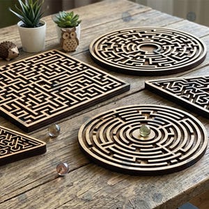 May include: Wooden maze puzzles in various shapes, including square, circular, and triangular, are displayed on a rustic wooden table. The puzzles are light brown with intricate maze designs. Decorative plants and marbles are also present.