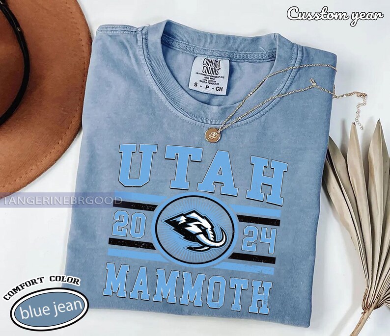 May include: A blue jean Comfort Colors t-shirt with the word "UTAH" in light blue block letters. Below the word "UTAH" is a circular logo with a mammoth graphic. The text "2024" and "MAMMOTH" are also printed on the shirt.