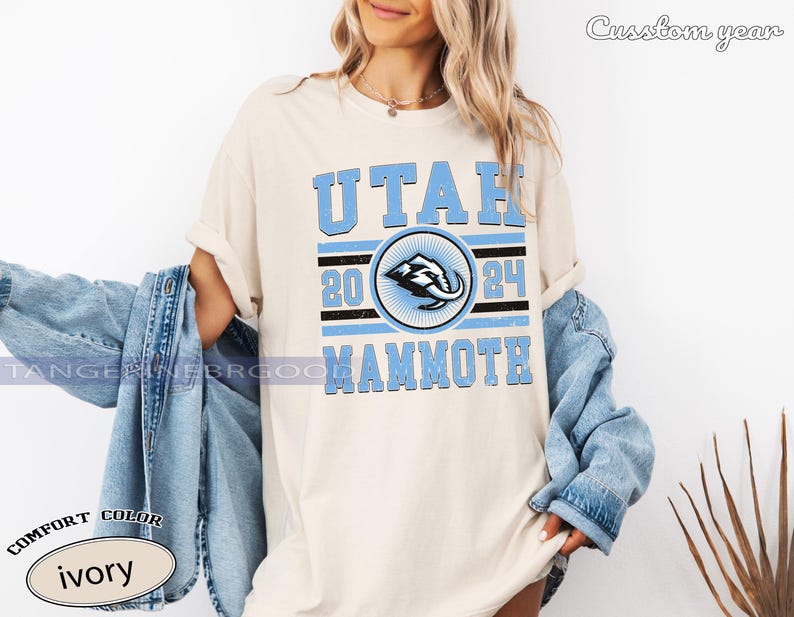 May include: Ivory-colored t-shirt with the text "UTAH 2024 MAMMOTH" in light blue. The design includes a circular emblem with a stylized mammoth graphic. The shirt is part of the "Comfort Color" collection.