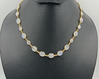 May include: A gold-toned necklace featuring oval, light-colored gemstones. The gemstones are linked together with small gold-colored connectors. The necklace is displayed on a black jewelry bust.