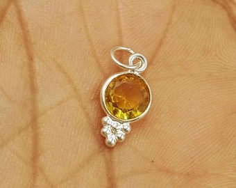 May include: A small, silver pendant with a round, golden-yellow gemstone. Below the gemstone is a cluster of smaller, silver-colored stones. The pendant is likely for a necklace or bracelet.
